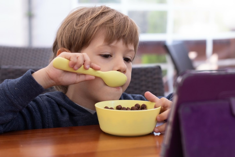 A child watches a show on a tablet while eating cereal